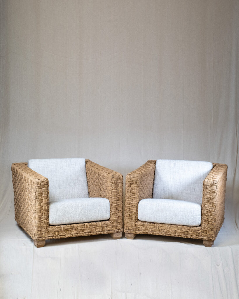 A pair of woven armchairs with white cushions.